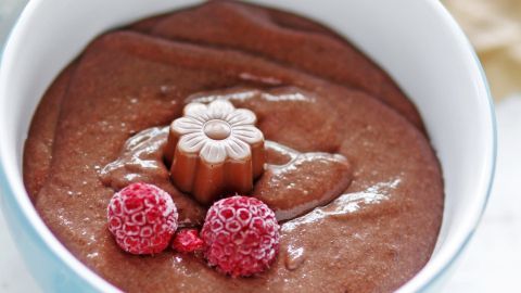 Eine cremige, kalorienarme Nutella wird in einer Schüssel präsentiert, dekoriert mit Himbeeren und einer Blume.