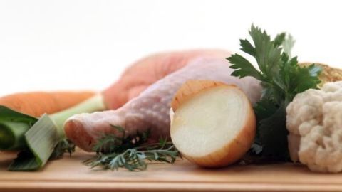 Hähnchenkeule auf Holzbrett mit Gemüse wie Zwiebel, Karotte, Lauch, Blumenkohl und Petersilie, ideal für Suppe.