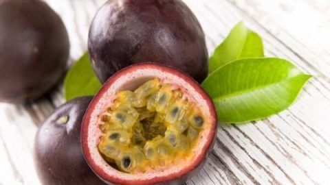 Eine geschnittene Passionsfrucht liegt auf einem Holzuntergrund, umgeben von blattgrünen Pflanzen.