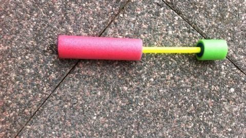 Eine bunte Wasserpistole liegt auf einem Kopfsteinpflaster, möglicherweise als Werkzeug, um Tauben zu vertreiben.