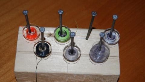 Sechs Nähmaschinenspulen stehen aufrecht in einem Holzständer, ordentlich aufbewahrt auf einem Tisch.