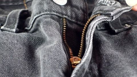 Ein geöffneter Reißverschluss an einer dunklen Jeans, der repariert wird, zeigt eine praktische Lösung für defekte Zipper.