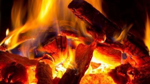 Glühende Holzscheite im Kaminofen erzeugen lebendige Flammen und Wärme, umgemgeben von einer gemütlichen, dunklen Umgebung.