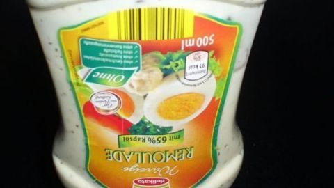 Eine Flasche Remoulade steht auf einem dunklen Tisch, bereit zum Benutzen. Der Text oben besagt "Kurzer Einstich".