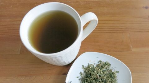 Eine Tasse mit Kräutertee steht neben einer kleinen Schale mit frischen Kräutern, ideale Unterstützung bei Frauenleiden.