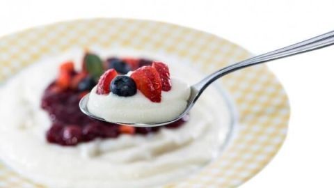 Ein Löffel Grießbrei mit frischen Beeren wird über einem Teller mit gelbem Karomuster gehalten.