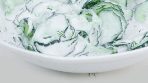 Gurkensalat mit Sahnesoße und Dill in einer weißen Schüssel, frisch serviert auf einem neutralen Hintergrund.