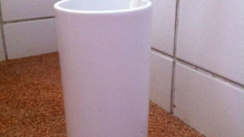 Eine weiße Blumenvase steht als WC Bürstenhalter auf einem korkähnlichen Untergrund im Badezimmer.