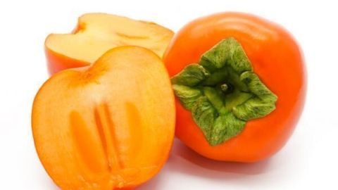 Die Kaki-Frucht, leuchtend orange, liegt zusammen mit einer halbierten Frucht auf einem weißen Hintergrund.