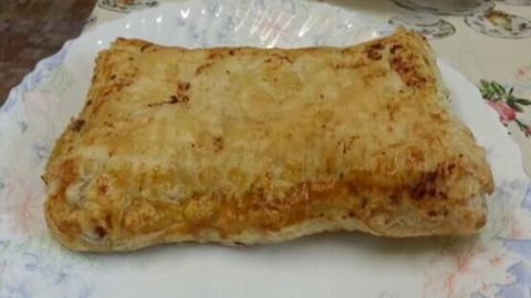 Ein harmonisch gebräunter Landtaschen, gefüllt mit Hackfleisch und Schafskäse, liegt ansprechend auf einem dekorativen Teller.