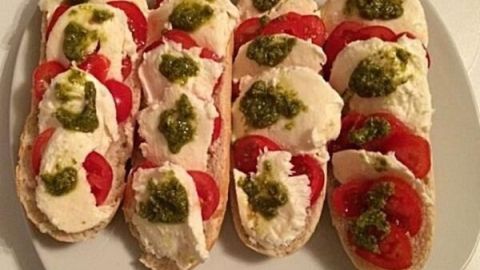 Auf einem Teller liegen mehrere Brötchen, die mit Tomaten, Mozzarella und Pesto belegt sind und frisch zubereitet wirken.