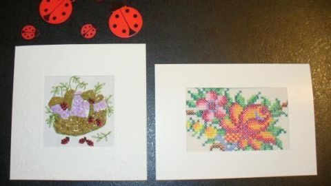 Zwei individuelle Grußkarten, links mit Blumen und Korb, rechts mit bunter Blume, auf Tisch platziert, umgeben von Marienkäfer-Dekorationen.