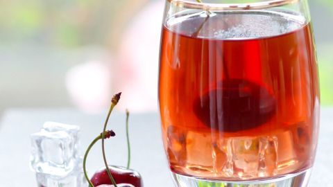 Ein elegantes Glas mit einem roten Drink und einer Kirsche, umgeben von Eiswürfeln und frischen Kirschen auf einem Tisch.