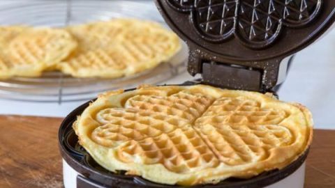 Ein Waffeleisen mit frisch gebackenen Waffeln steht auf einem Tisch, während im Hintergrund weitere Waffeln auskühlen.