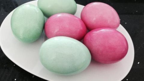 Bunte Ostereier liegen auf einem weißen Teller, gefärbt mit Lebensmittelfarben in rosa und grün, auf dunklem Hintergrund.