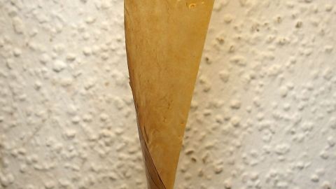 Ein klebriger Streifen von einer Fliegenfalle hängt an einer rauen Wand, während er sich zu lösen scheint.