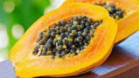 Zwei Hälften einer Papaya liegen auf einem Holztisch, im sonnigen Hintergrund verschwommenes Grün.