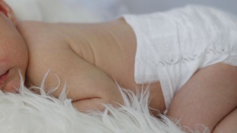 Ein schlafendes Baby liegt auf weichlichem, flauschigem Untergrund und zeigt einen kleinen, runden Po in einer Windel.