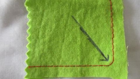 Grüner Stoff mit genähter roter Ecke und Pfeil, der das Ausformen im Schneiderei-Kontext anzeigt.