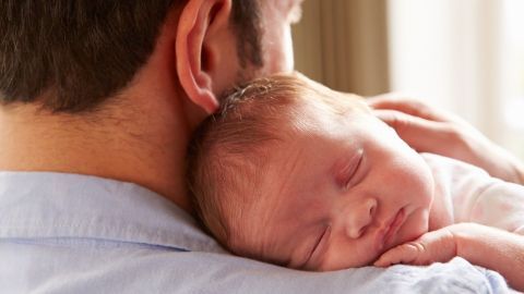 Ein schlafendes Baby liegt friedlich auf der Schulter eines Erwachsenen, umgeben von weicher, natürlicher Beleuchtung.