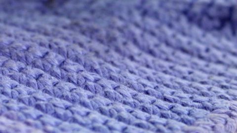 Ein gestrickter, lila Schal liegt sanft auf einer Oberfläche, bereit zum Verschenken oder für eine nette Verpackung.