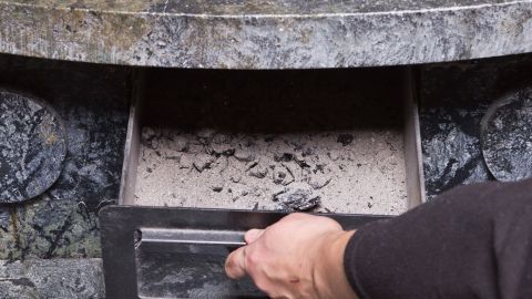 Eine Hand zieht eine Schublade mit Asche heraus, die für den Einsatz als Dünger für Pflanzen vorbereitet ist.