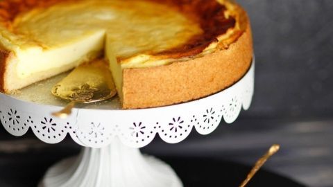 Ein kräftiger Käsekuchen mit Rosinen steht auf einem eleganten Kuchenteller, während ein Stück davon auf einem Teller serviert wird.