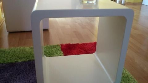 Ein weißer Lacktisch steht auf buntem Teppichboden, oben drauf ein Glas mit Kerze, im Hintergrund helle Holzböden.