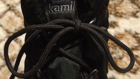 Ein schwarzer Schnürsenkel ist ordentlich gebunden an einem Schuh. Die Umgebung zeigt einen weichen, hellen Teppich.