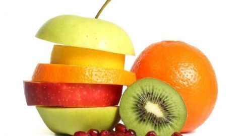 Früchte in Scheiben gestapelt: Apfel, Orange, Kiwi neben einer ganzen Orange und Granatapfelkernen auf weißem Hintergrund.