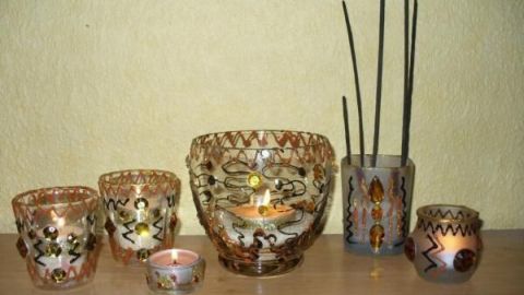 Schlichte Gläser stehen dekorativ auf einem Tisch, einige mit Kerzen, umgeben von bunten Materialien und einem ruhigen Hintergrund.