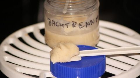 Ein Glas mit Backtrennmittel steht auf einem Gitter. Ein Spatel entnimmt eine Portion des mittelflüssigen Trennmittels.