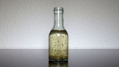 Eine klare Ölflasche steht auf einer glatten Oberfläche und reflektiert das Licht, während sie mit goldenem Öl gefüllt ist.