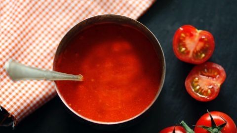 Eine Schüssel mit Tomatensauce steht in der Mitte, während frische Tomaten und ein kariertes Tuch daneben liegen.