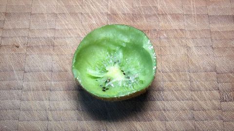 Ein aufgeschnittener Kiwi liegt auf einem Holzbrett. Die raue Oberfläche der Kiwi zeigt saftiges, grünes Fruchtfleisch.