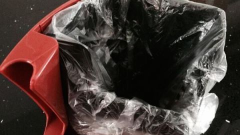 Ein roter Tresterbehälter mit einer durchsichtigen Plastiktüte darin steht auf einer dunklen Fläche, um Schimmel zu verhindern.