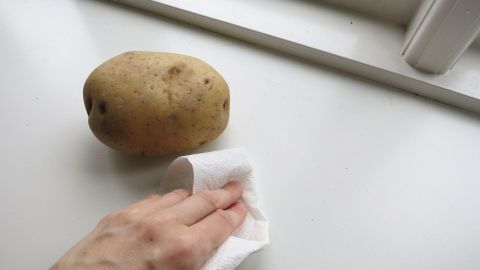 Ein Handtuch wischt über eine weiße Kunststofffläche, während eine Kartoffel daneben liegt, um zu reinigen.
