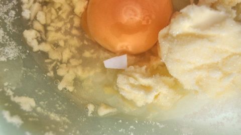 Ein aufgeschlagenes Ei mit Eierschalenstücken liegt zusammen mit Küchenzutaten in einer grünen Schüssel.