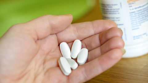 Eine Hand hält mehrere weiße Tabletten, die zur Linderung von Schmerzen in den Beinen nach dem Aufstehen gedacht sind.