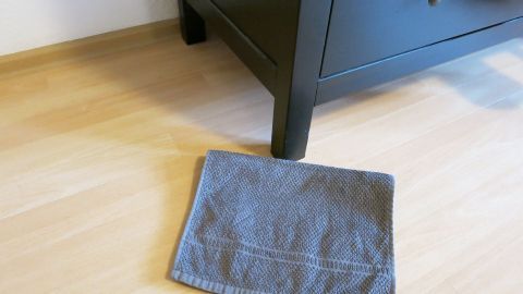 Ein Schrank wird auf einem Holzboden mit einem grauen Handtuch darunter vorbereitet, um schwere Gegenstände leichter zu transportieren.