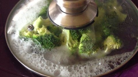 Ein bunter Dampfeinsatz kocht Brokkoli, während Blasen aufsteigen und der Dampf das Gemüse sorgfältig gart.