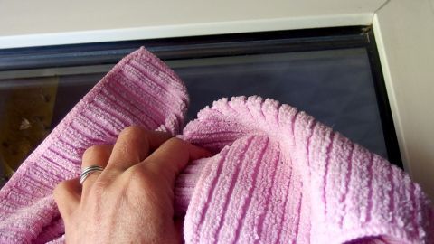 Eine Hand hält ein pinkes Reinigungstuch, während sie ein Fenster putzt, um Schmutz und Flecken zu entfernen.