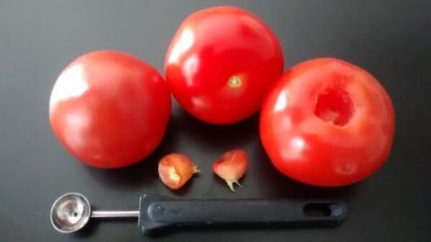 Tomaten liegen auf schwarzem Hintergrund. Eine Tomate ist entstrunkt, mit einem Küchengerät daneben und entferntem Strunk.