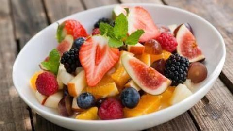 Eine Schüssel mit buntem Obstsalat, der frisch zubereitet und auf einer rustikalen Holzoberfläche präsentiert wird.