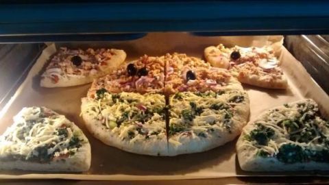 Tiefkühlpizzen backen im Ofen auf einem Blech; die Pizzen sind mit Oliven, Gemüse und Käse belegt.