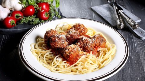 Fleischklößchen liegen auf Spaghetti, überzogen mit Tomatensauce und Parmesan, umgeben von frischen Zutaten wie Tomaten und Knoblauch.