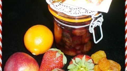 Ein Einmachglas mit eingelegtem Obst steht auf schwarzem Hintergrund, umgeben von frischen Früchten: Orangen, Erdbeeren und Aprikosen.