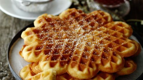 Eine stapelbare Portion lockerer Waffeln liegt auf einem Teller, umgeben von einer Schale mit roter Marmelade.