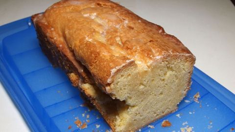 Ein Zitronenkuchen liegt angeschnitten auf einem blauen Tablett, umgeben von Kuchenkrümeln.