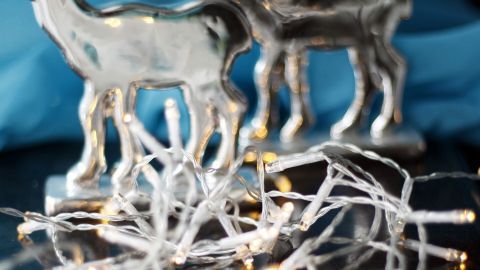 Eine Lichterkette liegt unordentlich auf einem Tisch, umgeben von silbernen Rehfiguren, vor einem blauen Hintergrund.
